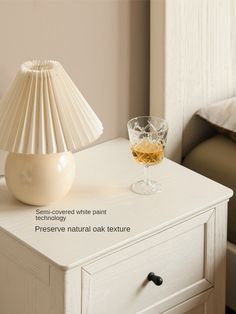 a white table with a glass of wine on it next to a lamp and bed