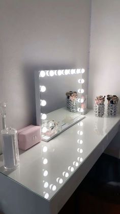 a vanity mirror with lights on top of it next to a bottle and vase filled with flowers