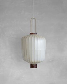 a white vase hanging from a string on a wall with a light fixture in the background