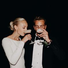 a man and woman standing next to each other drinking wine