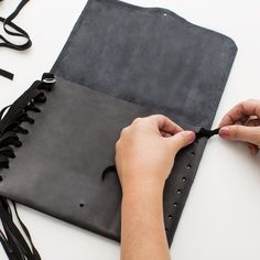 a person is cutting leather with scissors on a white table next to a black bag