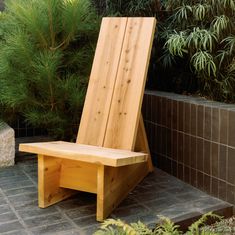 a wooden chair sitting on top of a stone floor next to a planter filled with green plants