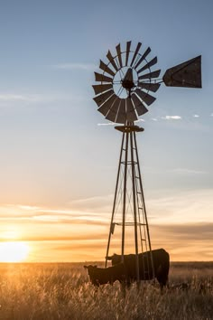 the sun is setting behind a windmill and two cows