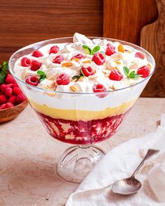 a dessert with fruit and whipped cream in a glass dish on a table next to strawberries