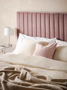 a bed with white sheets and pink headboard next to a lamp on a night stand