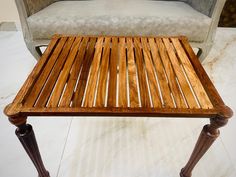 a wooden table sitting on top of a white floor next to a chair and ottoman