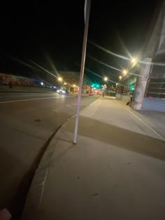 an empty street at night with no cars or people on the road and lights in the background