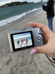 a person holding up a camera to take a photo on the beach with their friends