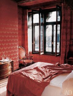 a bed sitting next to a window in a room with red wallpaper and curtains