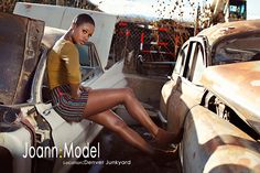 a woman sitting on the hood of an old car in front of rusted cars