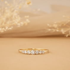 a yellow gold ring with five diamonds on it and a white flower in the background