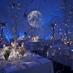 a room filled with lots of tables covered in white linens and decorated with trees