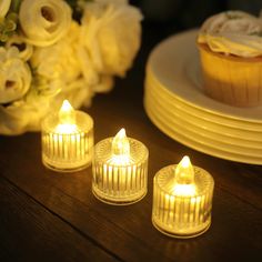 three lit candles sitting on top of a wooden table next to plates and cupcakes