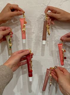 four hands holding different types of lip glosses on a white table with gold chains