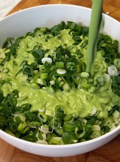 a white bowl filled with green vegetables on top of a wooden table next to chopsticks