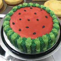 a watermelon cake with green icing and black dots on the top, surrounded by cookies