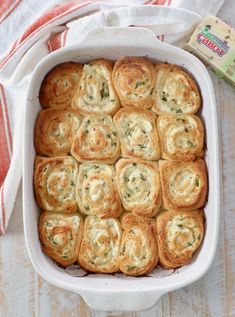 a casserole dish filled with spinach rolls next to a packet of crackers