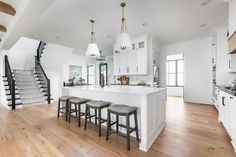 a large kitchen with white cabinets and wooden flooring next to an open stair case