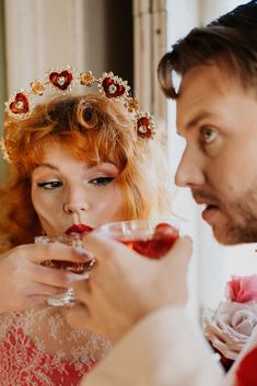 a man and woman dressed in fancy clothing holding wine glasses with strawberries on them