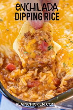 a hand holding a tortilla chip being dipped with chili and cheese in a casserole dish