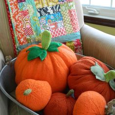 two orange pumpkins in a metal bowl on a chair next to a patchwork pillow