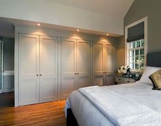 a large white bed sitting in a bedroom next to a wooden floor and two windows