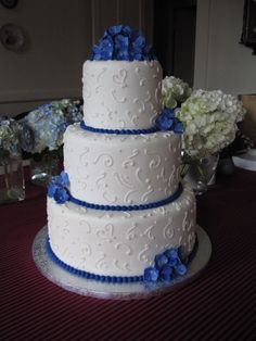 a three tiered white cake with blue flowers on the top and bottom, sitting on a table