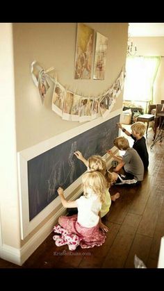 three children writing on a blackboard in front of a wall with pictures hanging above it