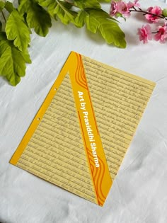 a piece of yellow paper sitting on top of a table next to some pink flowers