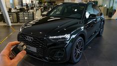 a person holding a car key in front of a black audi suv at an automobile dealership