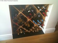 a wine rack filled with lots of bottles on top of a hard wood floor next to a white wall