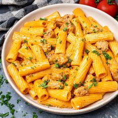 a white bowl filled with pasta and meat on top of a table next to tomatoes