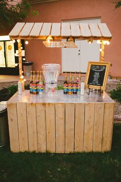 an outdoor bar is set up with liquor bottles and lights on the outside, along with a chalkboard sign