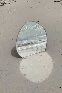 a round mirror sitting on top of a sandy beach next to the ocean's edge