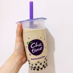 a hand holding up a drink in front of a white wall with the word cha time on it