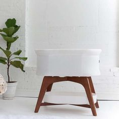 a white ottoman sitting next to a potted plant on top of a wooden stand