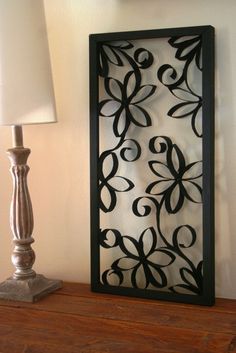 a lamp sitting on top of a wooden table next to a metal wall panel with flowers