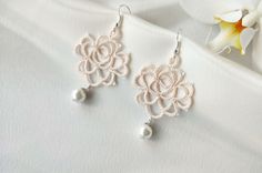 a pair of white earrings with pearls hanging from it's earwires next to a flower