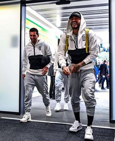 two men walking through an airport with one wearing a white hoodie and the other in grey sweatpants