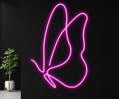 a purple neon bird on a black wall next to a potted plant