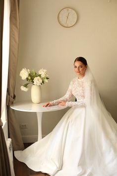 a woman in a wedding dress sitting at a table next to a vase with flowers