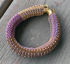 a purple and gold beaded bracelet sitting on top of a wooden table