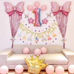 a pink and gold 1st birthday party set up with balloons, streamers, confetti, and a couch