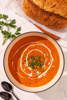 a bowl of tomato soup next to a loaf of bread on a white counter top