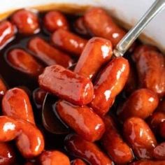 hot dogs are being cooked in a white bowl with sauce on the side and a spoon sticking into them