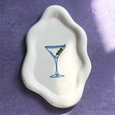 a white plate with a blue rim and a martini glass painted on the side, against a purple background