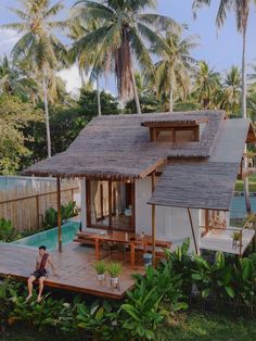 a person sitting on a wooden deck in front of a house with a pool and palm trees