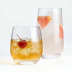 two glasses filled with liquid and fruit next to each other on a white table top