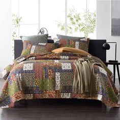 a bed covered in a multi colored patchwork comforter set with pillows and blankets