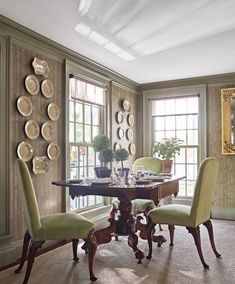 a dining room table and chairs with plates on the wall behind them in front of two windows